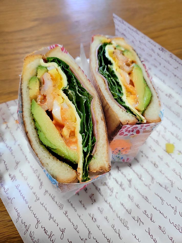 Homemade shrimp and avocado sandwich wrapped in paper and cut in half, showing the layers inside